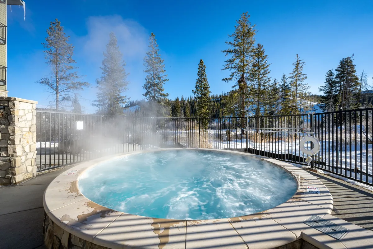 A serene exterior shot capturing a hot tub nestled among surrounding trees with a stunning mountain view. The setting is peaceful and inviting, ideal for morning sunrises or nighttime stargazing amidst the crisp mountain air.