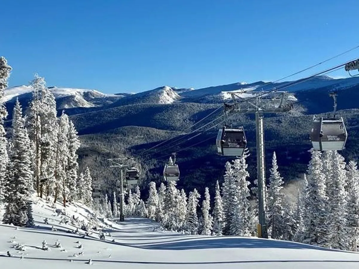 An exhilarating exterior shot featuring a ski lift rising above snow-covered trees with a dramatic mountain range backdrop. Skiers and snowboarders traverse the slopes below, capturing the thrill of mountain adventures and the breathtaking beauty of the Rockies during winter.