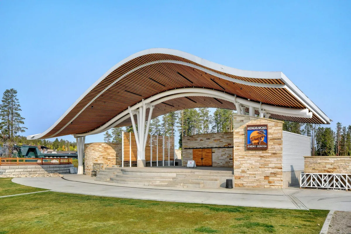 The Hideaway Park amphitheater with its unique curved roof and stone facade stands ready for concerts or community events. Event signage is visible, and the setting suggests a place for memorable live music and outdoor festivities.