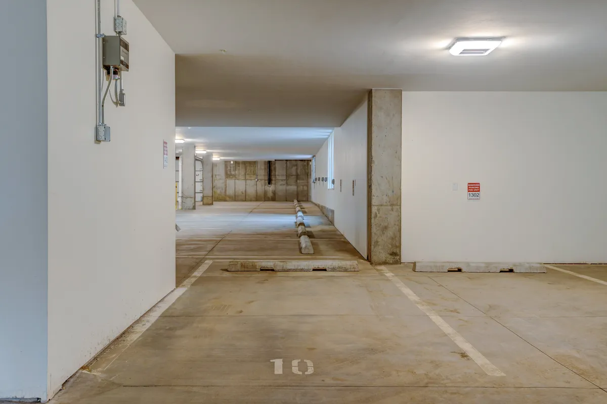 The image shows a well-lit, heated underground parking garage with clearly marked spaces, modern concrete walls, and pedestrians moving to and from their vehicles. The scene emphasizes ease of arrival, convenience, and security for guests returning from a day of adventure.