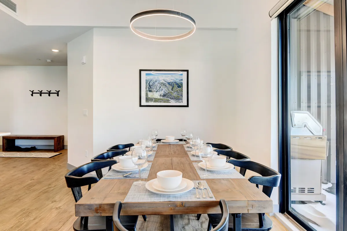 A long, elegant wooden dining table under a stylish suspended light fixture, enhanced by framed mountain-inspired artwork. The scene sets the stage for family feasts, celebrations, and cozy breakfasts, with ample seating for group gatherings.