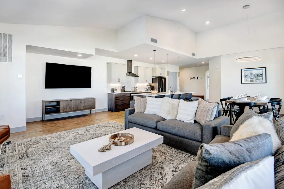 A contemporary living room setting with a plush sofa, coffee table, expansive television, and a view into the adjacent dining area. The atmosphere is cozy and inviting, ideal for movie nights, entertaining guests, or casual family relaxation after a day outdoors.