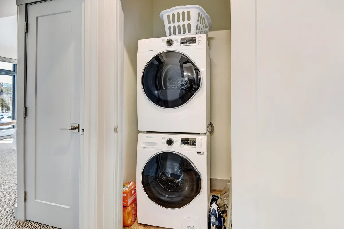 A neat laundry area featuring a stacked washer and dryer with a laundry basket ready for use. The setting is functional yet thoughtfully designed, making daily routines effortless for guests.