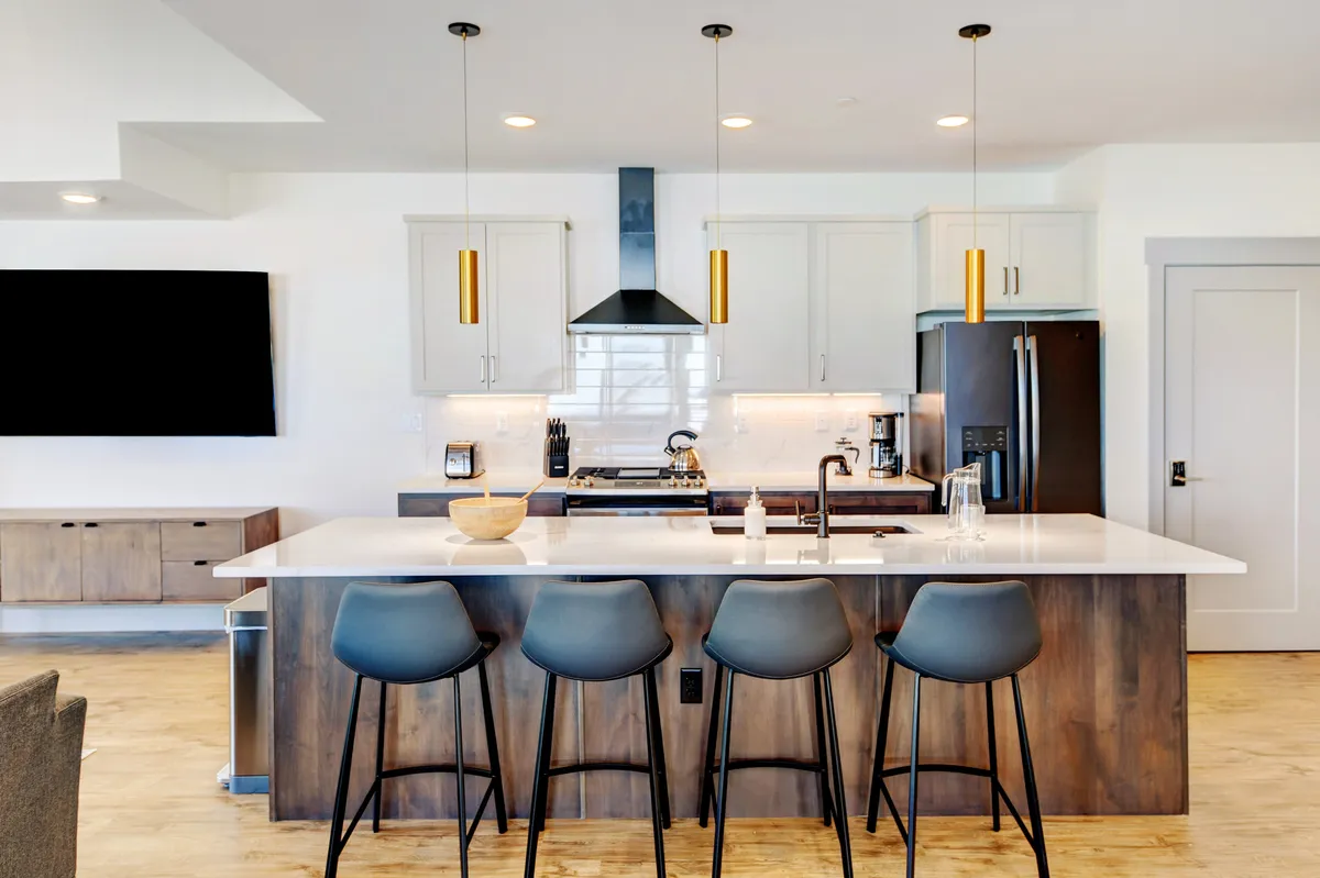 The image showcases a sleek, contemporary kitchen with a spacious island, stylish pendant lights, modern appliances, and inviting bar stools—ideal for gatherings, meals, and memorable moments with family and friends.